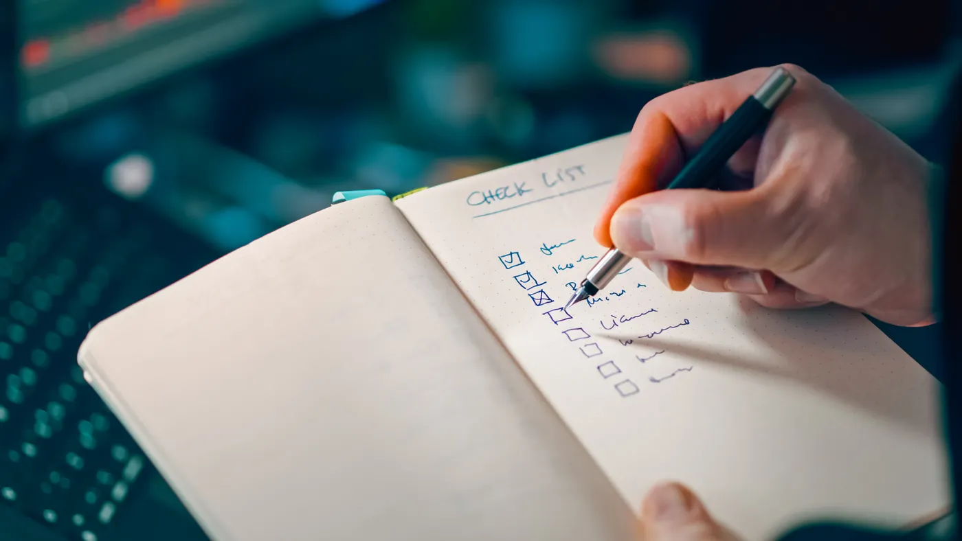 Close-up of a hand writing in a notebook with a checklist for effective task management.