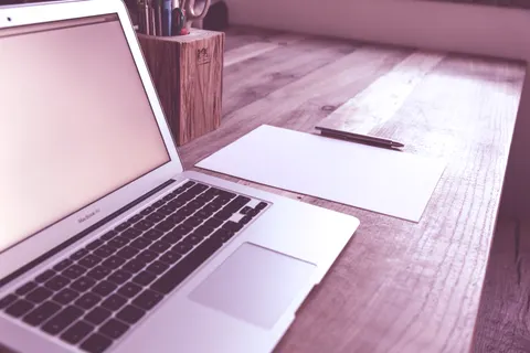 A clean and organized desk with a laptop, paper, and pen, ideal for productivity.